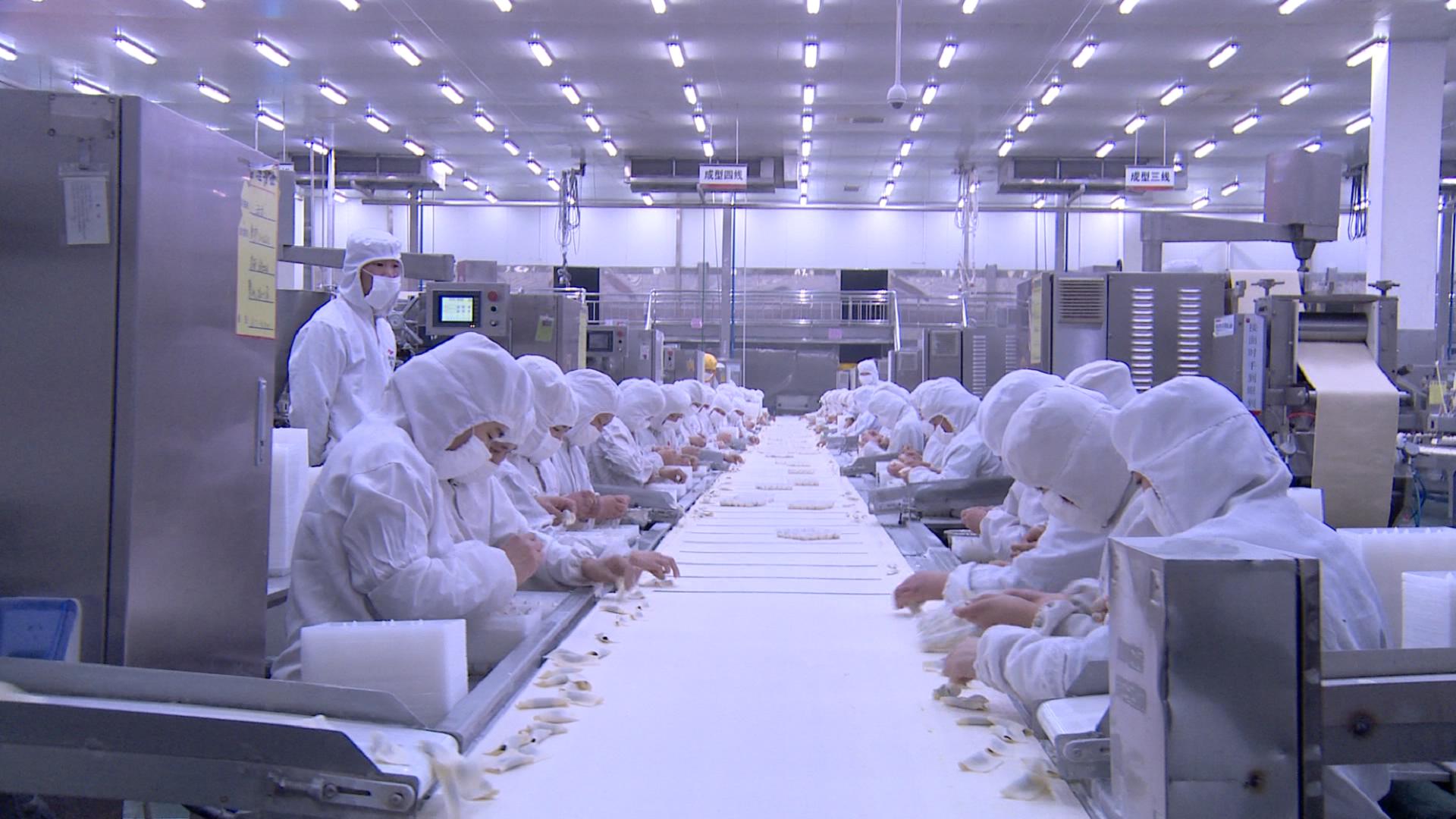 在水饺生产车间里,身穿白色无菌服的工人,戴着口罩分坐在生产流水线